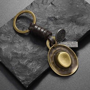 Vintage braided leather cowboy hat keychain with engraved metal plates on stone background