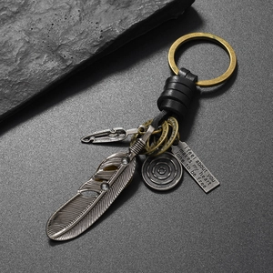Detail of vintage leather keychain with bronze feather charm and engraved metal pendant