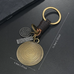 Detail view of woven brown leather keychain with bronze ginkgo leaf and vintage metal plate