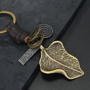 Macro detail of bronze ginkgo leaf keychain with leather strap and engraved metal plate