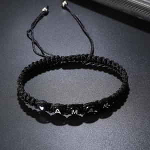 Detail of adjustable black woven bracelet featuring AMAM letters and heart beads