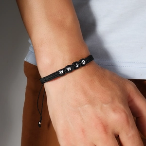 Close-up of a hand wearing a black woven WWJD letter bead bracelet with adjustable cord