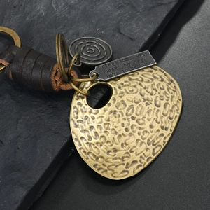 Detailed macro view of vintage bronze ginkgo leaf keychain with woven leather and metal charms