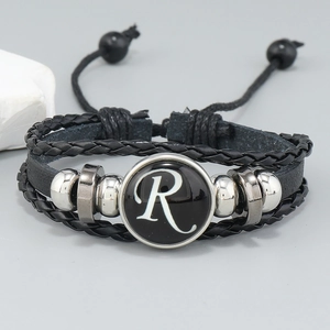 Macro shot of multilayer leather bracelet featuring letter R glass charm and braided cords