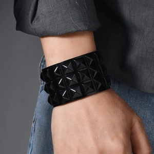 Detail of a black punk leather bracelet featuring three rows of polished pyramid studs