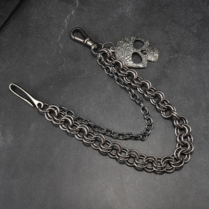 Detail of double-layer punk pants chain with engraved skull pendant on dark stone surface