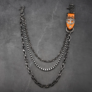 Détail d'une chaîne de pantalon triple en métal gris et cuir orange avec croix