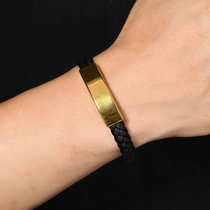Primer plano de una pulsera de cuero trenzado negro con una placa de metal dorado pulido