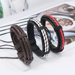 Dettaglio di tre braccialetti in pelle intrecciata multistrato nei toni marrone e nero
