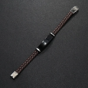 Detalle de una pulsera de cuero trenzado marrón con placa de metal negro y cierre plateado