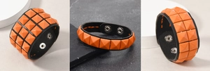 Details von orangefarbenen Pyramidennieten auf schwarzem Lederarmband mit Druckknopfverschluss