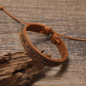 Vintage brown leather woven bracelet with metal beads on a natural wood background