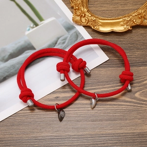 Detail of adjustable red braided couple bracelets with magnetic heart charms and metal ends