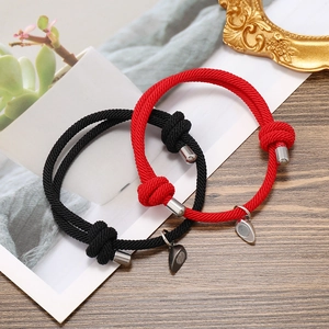 Detailed view of woven couple bracelets with magnetic heart charm on a rustic background