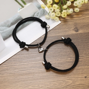 Close-up of black braided couple bracelets with a magnetic heart clasp on wooden surface