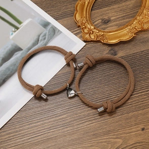Detail of khaki braided couples bracelets with magnetic heart charm on wooden desk