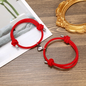 Detail of red braided couple bracelets featuring a magnetic heart-shaped silver metal clasp