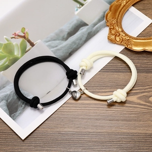Detail view of woven couple bracelets with magnetic heart charm on wooden background