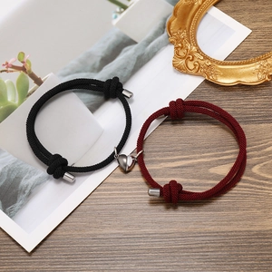 Detail of magnetic heart clasp on braided couple bracelets over a wooden background