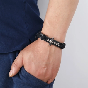 Détail d'un bracelet en cuir tressé vintage avec pendentif croix en argent au poignet