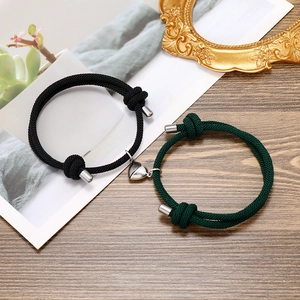 Close-up of woven couple bracelets with heart-shaped magnetic clasp on a wooden surface
