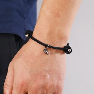 Detail of adjustable black braided rope bracelet with magnetic heart charm and silver beads