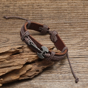 Vintage brown leather wrap bracelet featuring a silver double axe charm on aged wood background