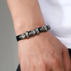 Close-up of a punk leather bracelet featuring four vintage silver skull charms on the wrist