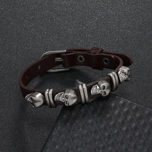 Detail of punk leather bracelet with silver skull charms and buckle closure on dark texture