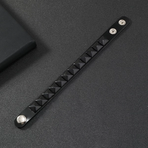 Close-up of black punk wristband featuring a row of pyramid studs and metal snap buttons