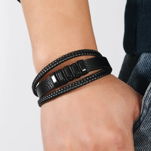 Detalle de una pulsera multicapa para hombre de cuero negro trenzado con cilindros metálicos