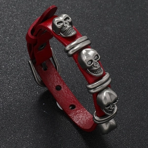 Detail of red punk leather bracelet with silver skull charms and needle buckle design