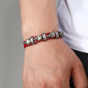 Close-up of red leather punk bracelet featuring four silver metal skull charms on wrist