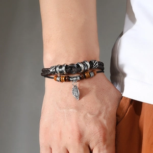 Macro detail of men's layered leather bracelet featuring leaf pendant and tiger eye beads