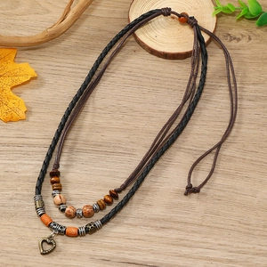 Vintage layered woven necklace with heart pendant and wooden beads on wood background