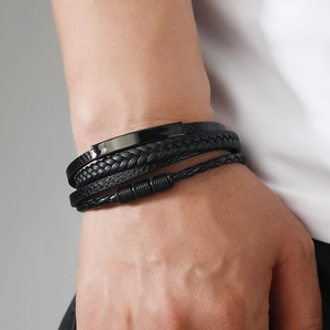 Close-up of men's multi-layer braided black leather bracelet with polished metal plate