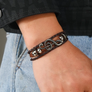 Close-up of men's leather bracelet featuring a vintage treble clef charm and metal beads