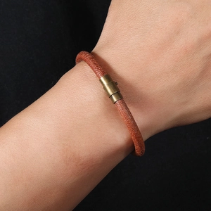 Close-up of a brown leather braided wristband with a vintage brass magnetic buckle