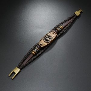Detail showing woven leather layers with a vintage golden tree of life charm on the bracelet