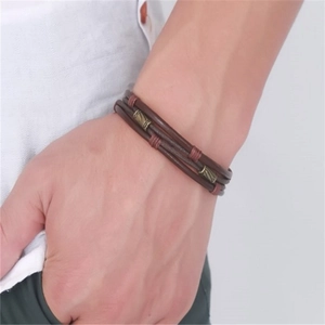 Primer plano de pulsera de cuero trenzado multicapa con tubos de metal vintage en la muñeca