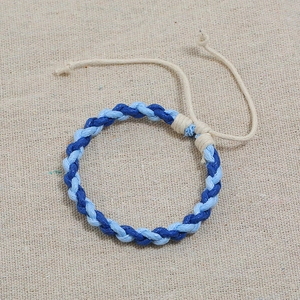Macro detail of hand-woven blue cotton cord bracelet with adjustable knot on linen back