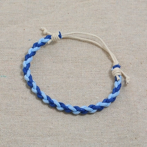 Detail of hand-woven cord bracelet showing blue spiral texture on linen background