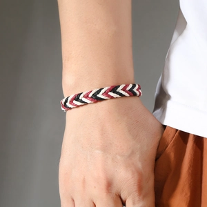Detail van een handgeweven waxkoord armband in rood zwart en wit om de pols van een man