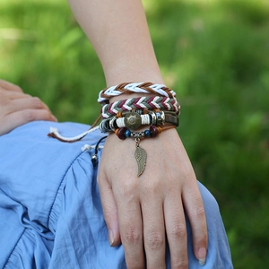 Detail of bohemian layered woven leather bracelets with metal wing charm on a natural background