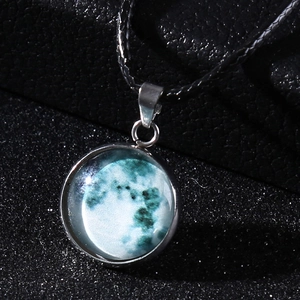 Macro shot of cosmic blue moon glass pendant with wax cord on a starry background
