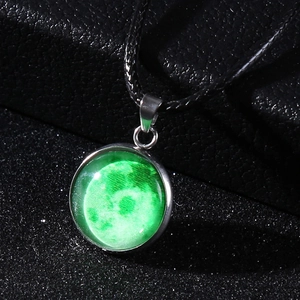 Macro view of glowing moon pendant with green glass cabochon on black woven cord