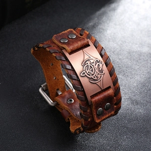 Macro shot of brown leather punk bracelet featuring a bronze dragon emblem and woven edges