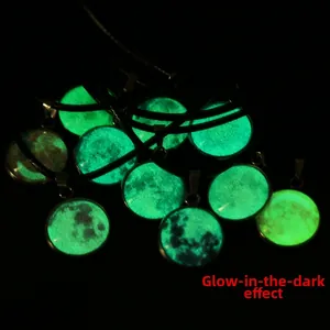Close-up of luminous moon pendant glowing green in dark background with metallic base