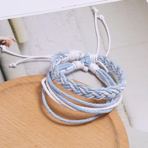 Détail de bracelets tressés bleu clair et blanc posés sur un support en bois naturel