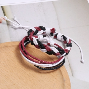 Détail de bracelets tissés faits main en noir, blanc et bordeaux sur un plateau en bois